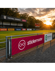 Sponsorbord met full colour bedrukking langs een voetbalveld tijdens zonsondergang op een professioneel sportpark.