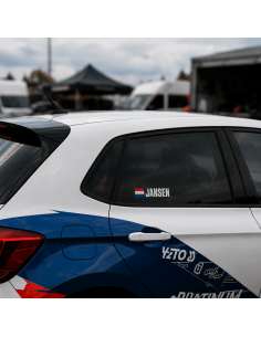 Rally naamsticker met vlag op de zijruit van een rallyauto in een paddockomgeving